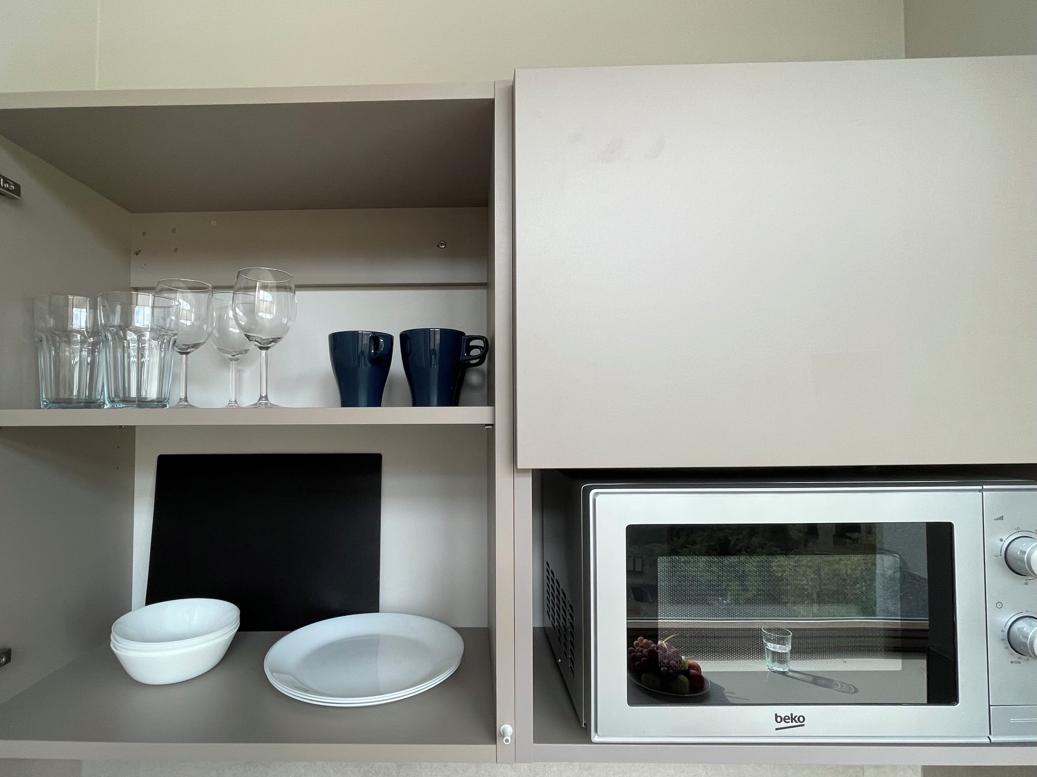 Una kitchenette con microondas, estantería con cristalería y un armario negro.