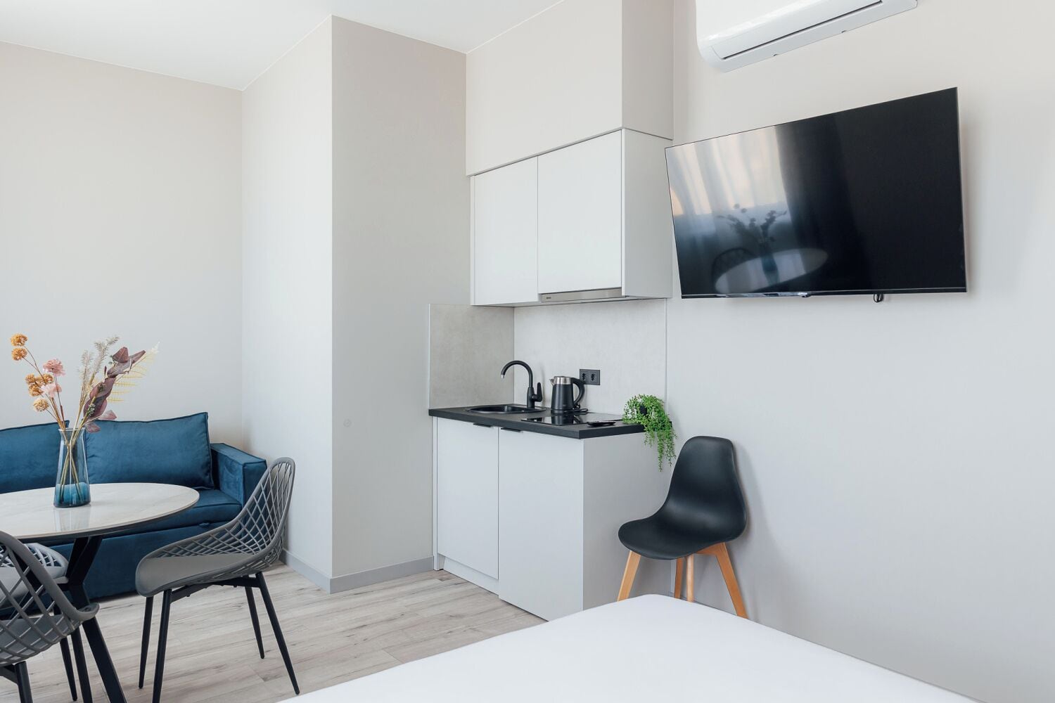 A modern kitchen with a flat-screen TV, a dining area with a round table and chairs, and a blue sofa.