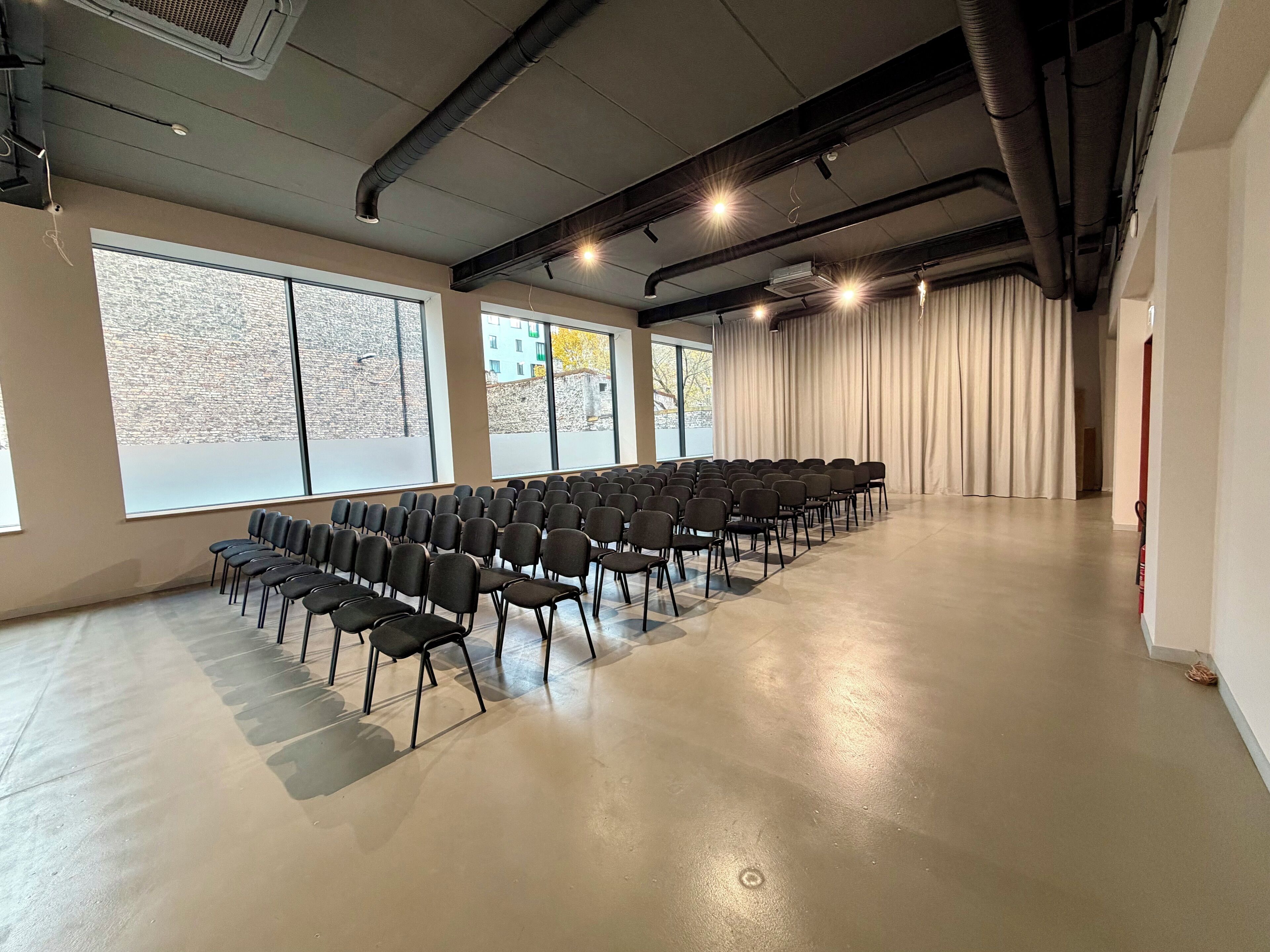 A conference room with rows of chairs, large windows, and a fire extinguisher.