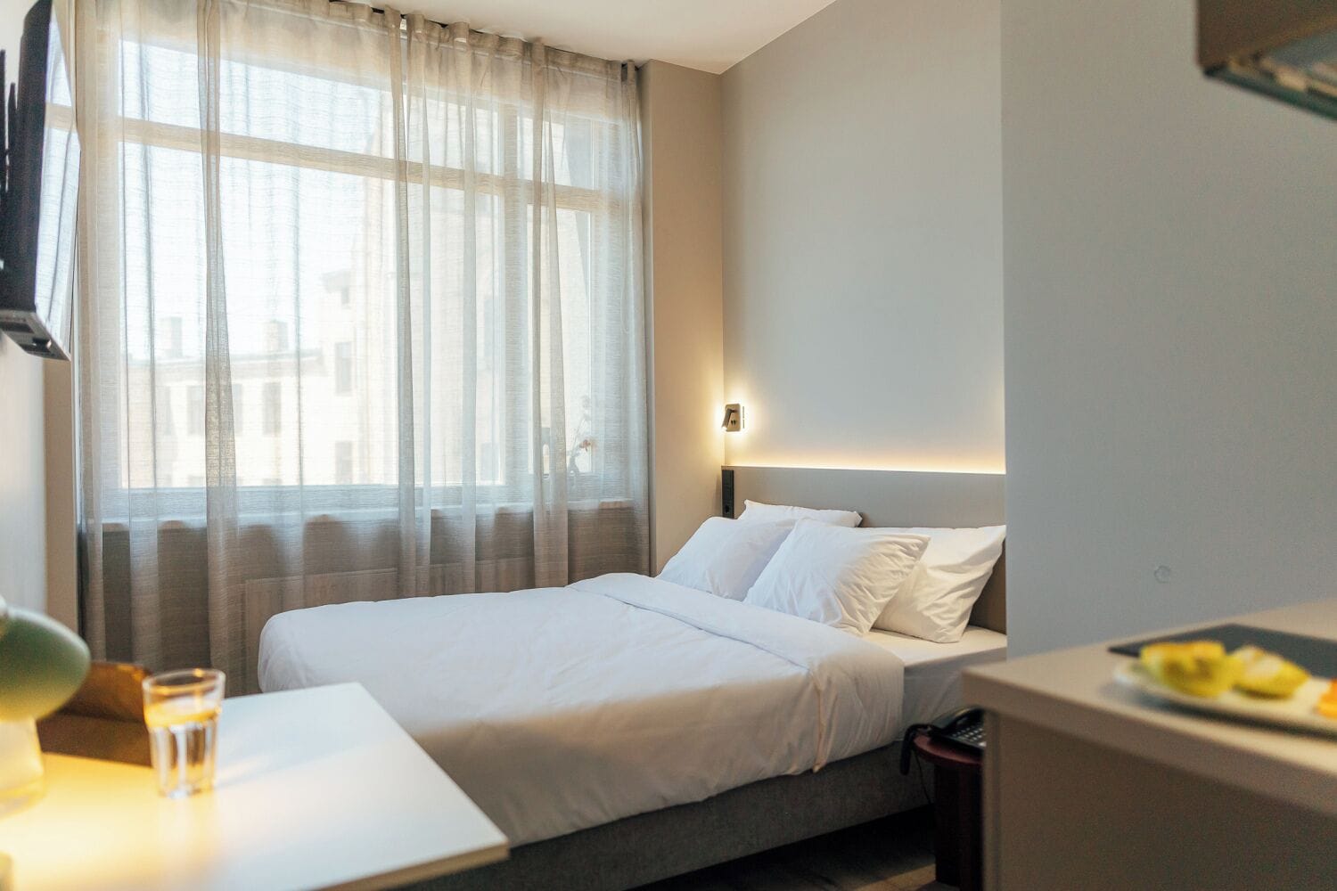 Een hotelkamer met een bed, nachtkastje met een glas water, een lamp en een schaal fruit.
