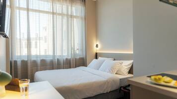 Een hotelkamer met een bed, nachtkastje met een glas water, een lamp en een schaal fruit.
