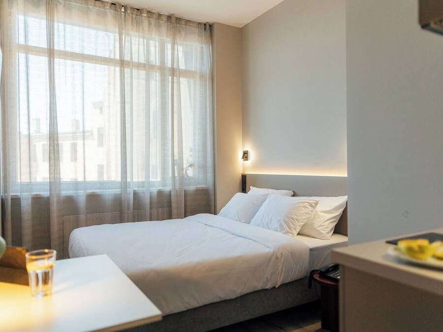A hotel room with a bed, a bedside table with a glass of water, a lamp, and a plate of fruit.