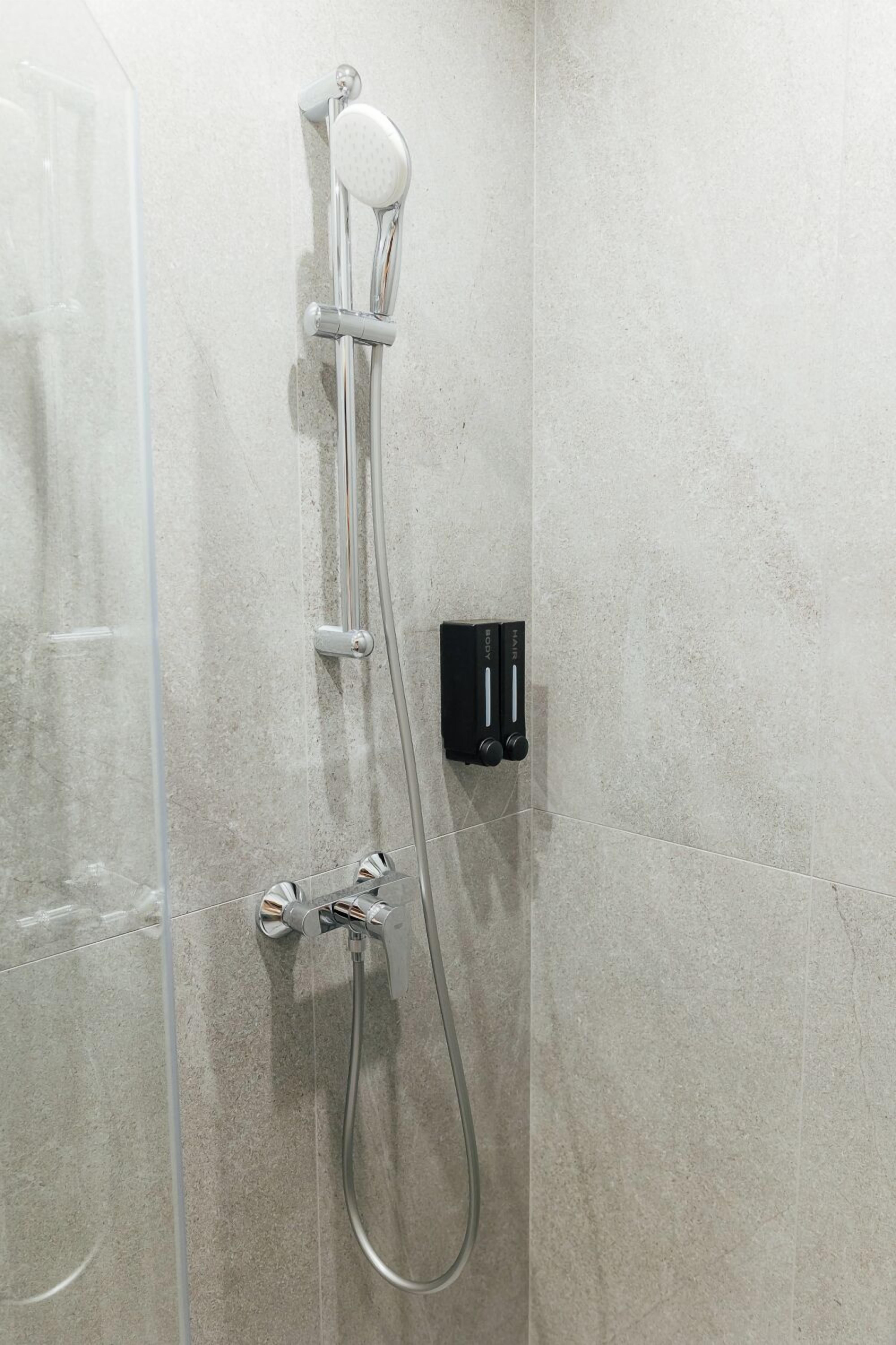 Una ducha con cabezal de ducha de mano y panel de control en la pared.