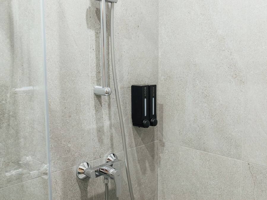 Una ducha con cabezal de ducha de mano y panel de control en la pared.