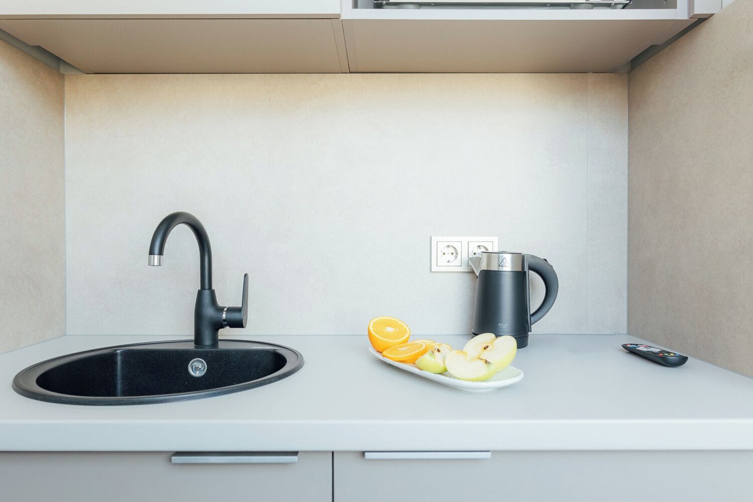 Una cocina con un lavamanos negro, una tetera y un plato con rodajas de fruta.