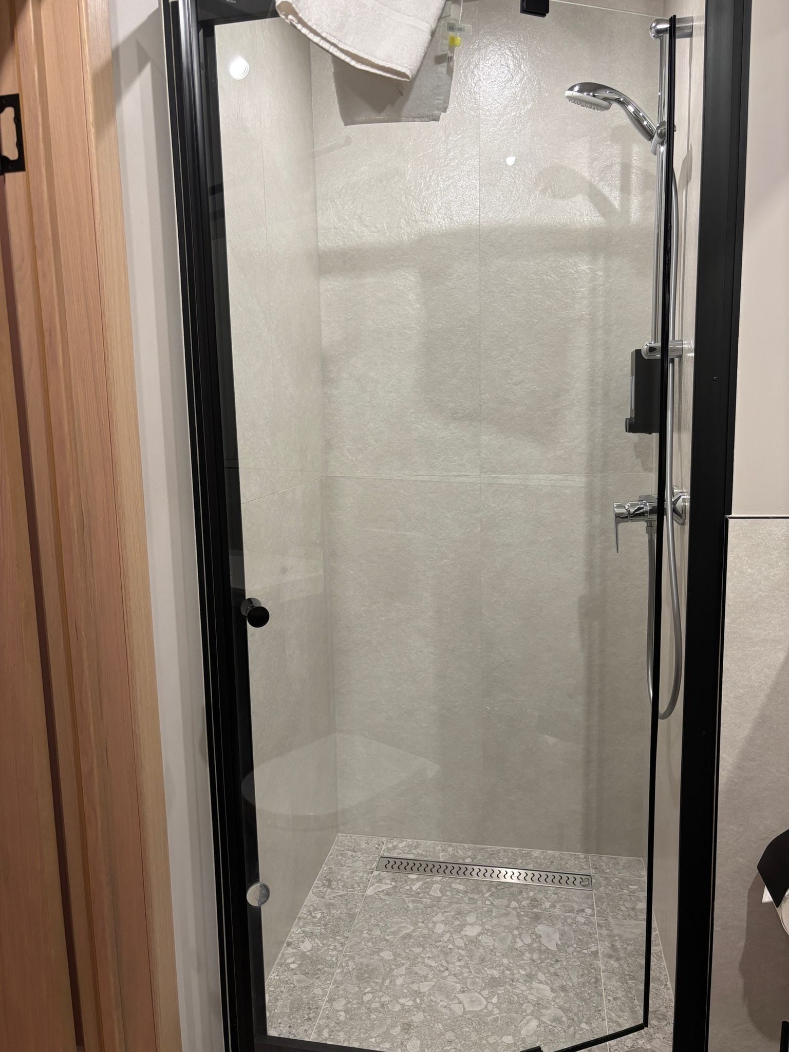 A glass-enclosed shower with a handheld showerhead and a wall-mounted faucet.