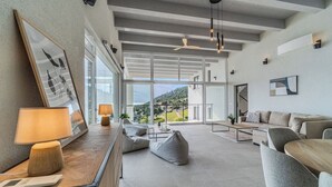 A modern living room with a sofa, a coffee table, and a view of a mountainous landscape through large windows.
