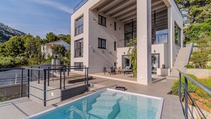 A modern two-story house with a rooftop pool, outdoor seating, and a staircase leading to a balcony.
