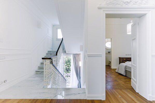 A staircase with white railings and a marble floor leading to a bedroom with a bed and a nightstand.