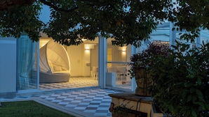 Un espacio al aire libre moderno con una zona de estar, suelo a cuadros, un asiento cubierto y una puerta de cristal que da a un espacio interior.