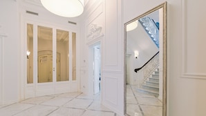 Un pasillo con piso de mármol, puertas blancas y un espejo grande que refleja una escalera.