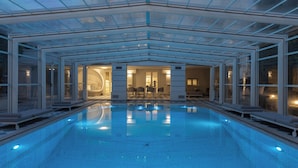 Una piscina interior moderna con paredes de vidrio, una zona de estar y un interior bien iluminado.