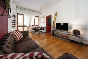 Un salon avec un canapé, un téléviseur posé sur un meuble, un coin repas avec une table et des chaises, et un mur d’accent de couleur rouge.