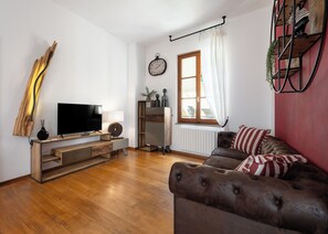 A living room with a TV, wooden furniture, a clock, a window with curtains, and a red accent wall. - Beautiful quiet and comfortable apartment in the center 8 minutes walk from the cathedral (Firenze)