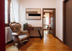 A hallway with a wooden floor, a chair with a leopard print, a desk with a plant, and a door leading to another room. - Beautiful quiet and comfortable apartment in the center 8 minutes walk from the cathedral (Firenze)