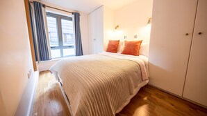 Un dormitorio con cama, ventana con cortinas, lámpara de noche y armario.