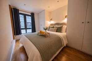 Una habitación de hotel con cama, mesita de noche y ventana con cortinas.