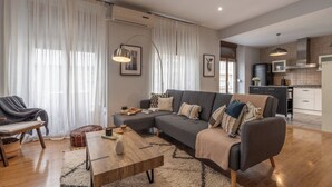 A modern living room with a sofa, coffee table, and a dining area with a chair and ottoman. - Cozy Home Casa Laura (Granada)