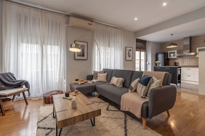 Een moderne woonkamer met een bank, salontafel en een eethoek met een stoel en poef.