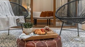 A cozy seating area with two black chairs, a small table with a tray of croissants, a cup, and a plant. - Calma Center Granada (Granada)