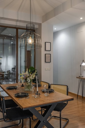 Een eetruimte met een houten tafel voor vier personen, zwarte stoelen, een hanglamp en een bloevas.