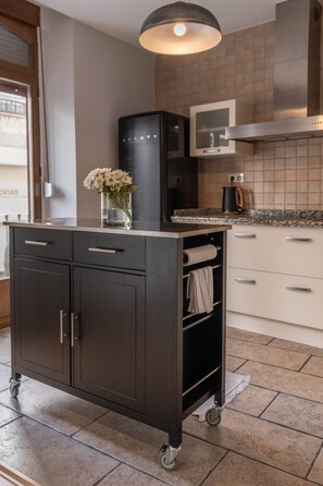 A kitchen with a dark-colored cabinet, a small table with a vase of flowers, and a tiled backsplash. - Cozy Home Casa Laura (Granada)