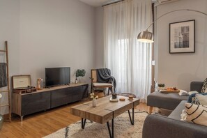 A modern living room with a flat-screen TV, wooden furniture, a coffee table, and a large window with curtains. - Cozy Home Casa Laura (Granada)