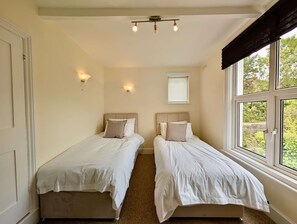 A room with two beds, a window with blinds, a ceiling light fixture, and a door. - Charming Two-Bedroom House in London (Greater London)