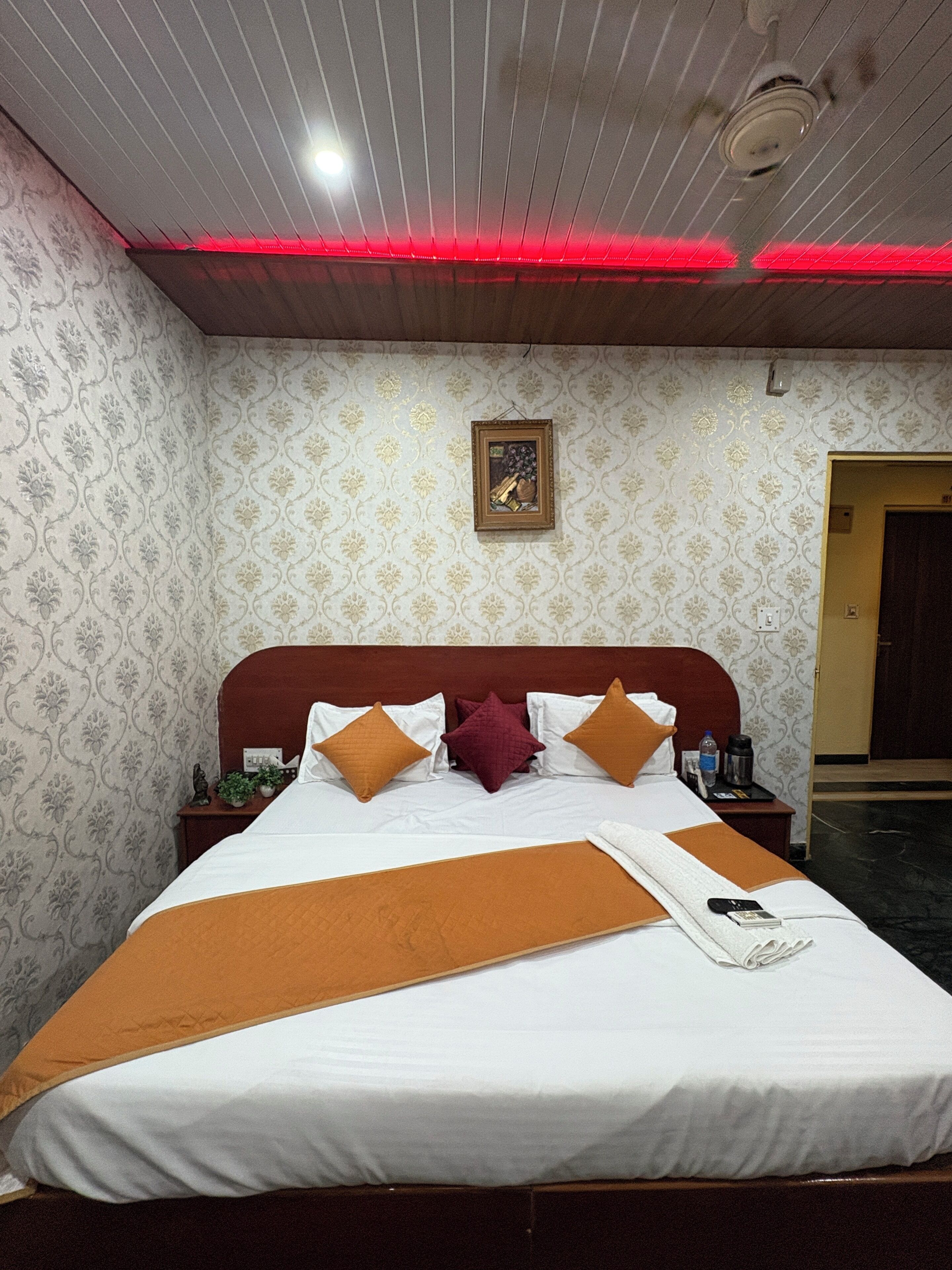 A neatly made bed with a white and brown bedspread, a wooden headboard, and a red ceiling light.
