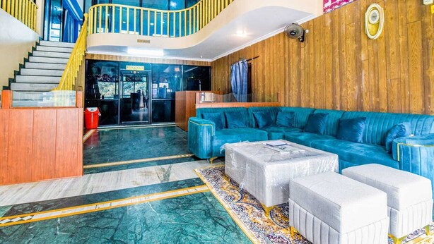 Eine großzügige Lobby mit einem blauen Sofa, einer Treppe mit gelb gestrichenen Geländern und einer Holzwand mit Wandgemälde.