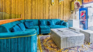 Ein Zimmer mit einer Holzwand, einem blauen Sofa, einem gemusterten Teppich und einem Pepsi-Kühlschrank.