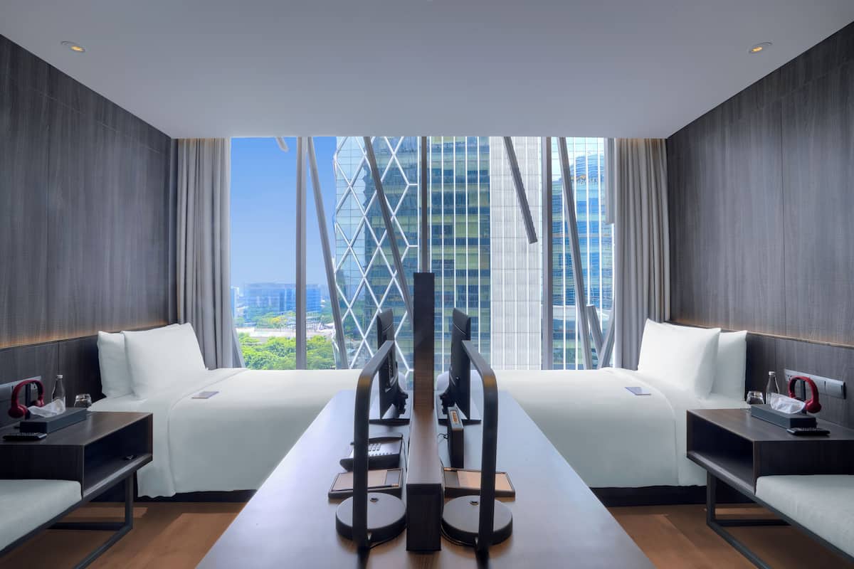 Una habitación de hotel moderna con un amplio ventanal, un escritorio con computadora y una cama con ropa blanca.