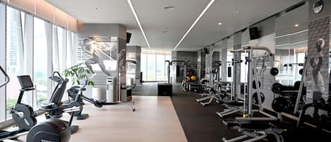 Un gimnasio moderno con máquinas de cardio, equipo de levantamiento de pesas y un espejo grande.