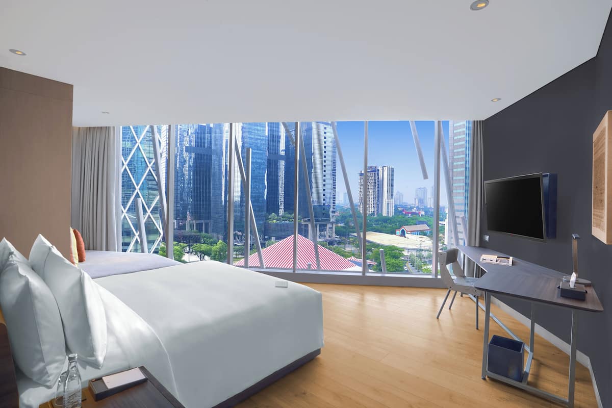 Habitación de hotel moderna con una cama grande, un escritorio y un televisor. Ofrece vistas de la ciudad a través de amplias ventanas.