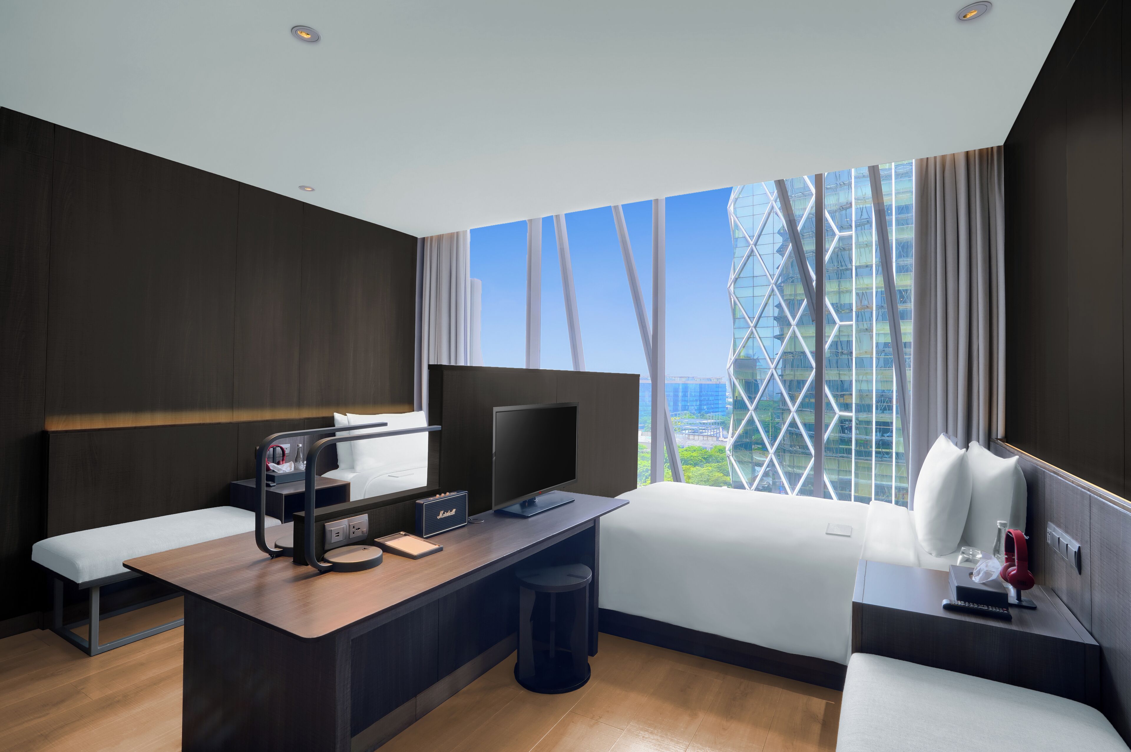 Une chambre d’hôtel moderne équipée d’un bureau, d’une télévision à écran plat, d’un lit et d’une grande fenêtre donnant sur la ville.
