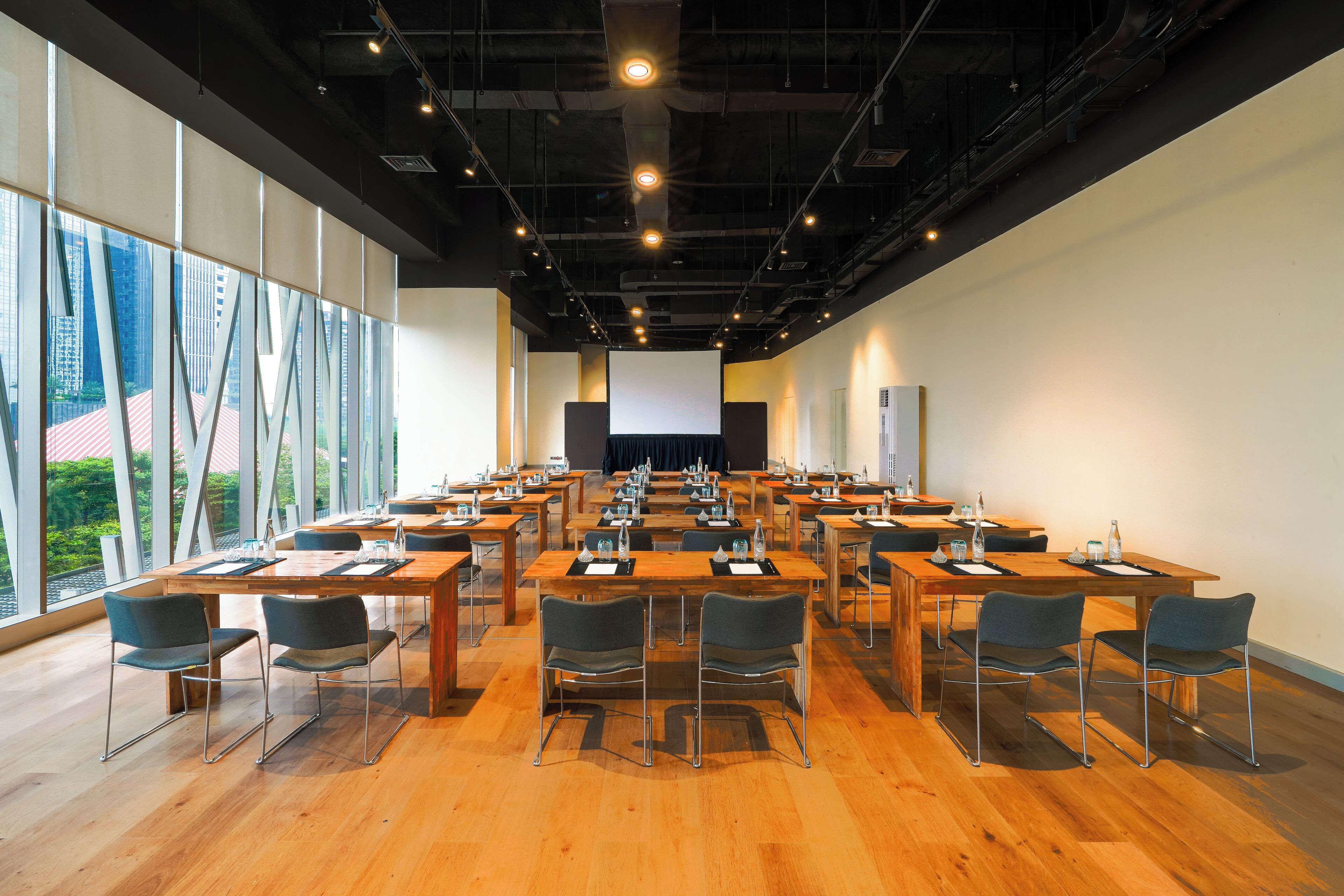 A conference room with multiple tables and chairs, large windows, and a projector screen.