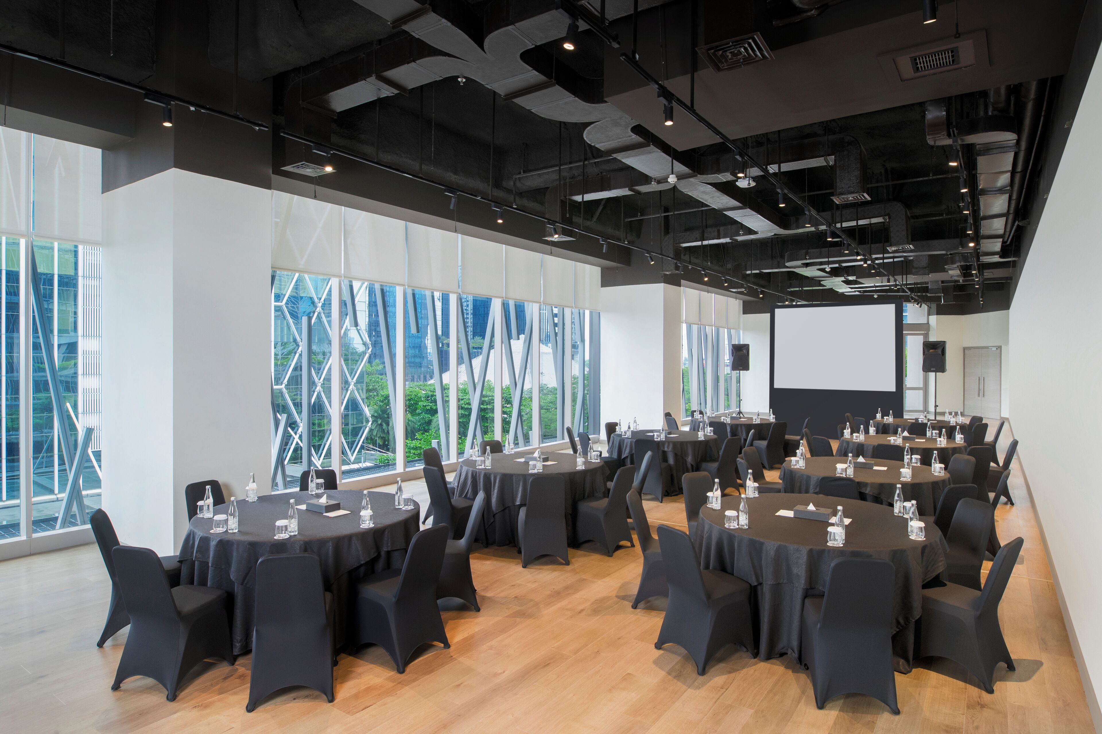 A conference room with multiple tables, chairs, and a projector screen.