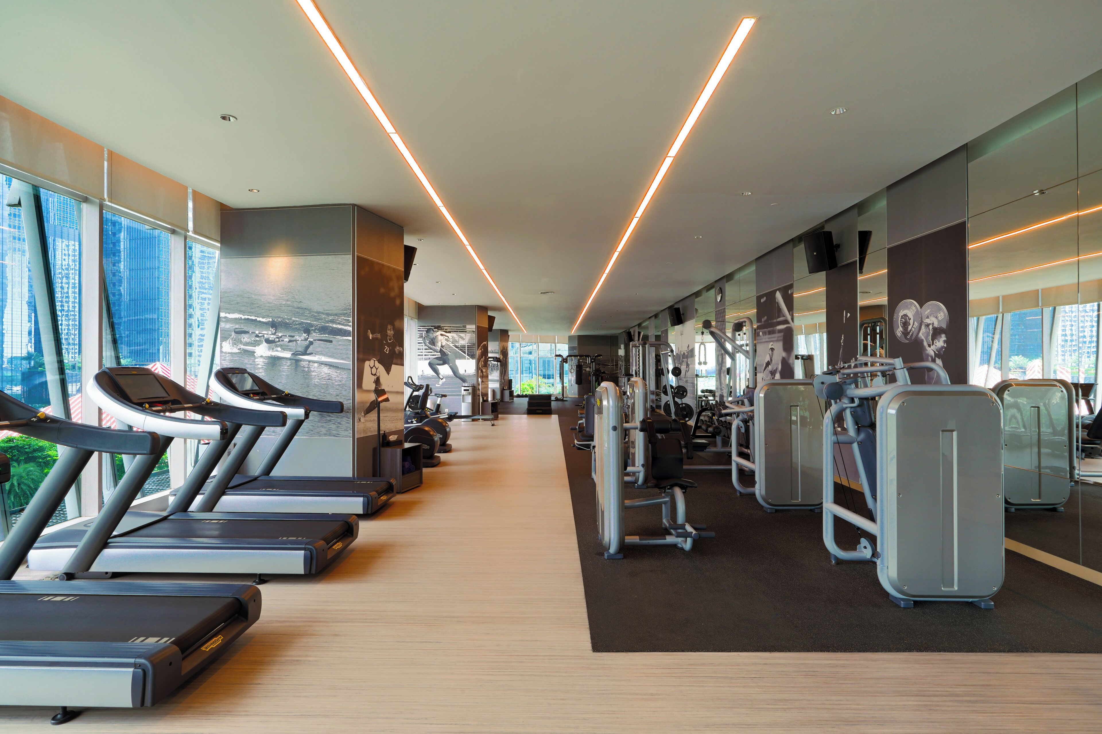 A modern gym with treadmills, weight machines, and large windows offering city views.
