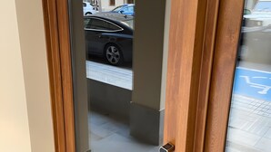 Puerta con panel de vidrio, cerradura electrónica y vista a la calle con coches estacionados y un edificio con grafitis.