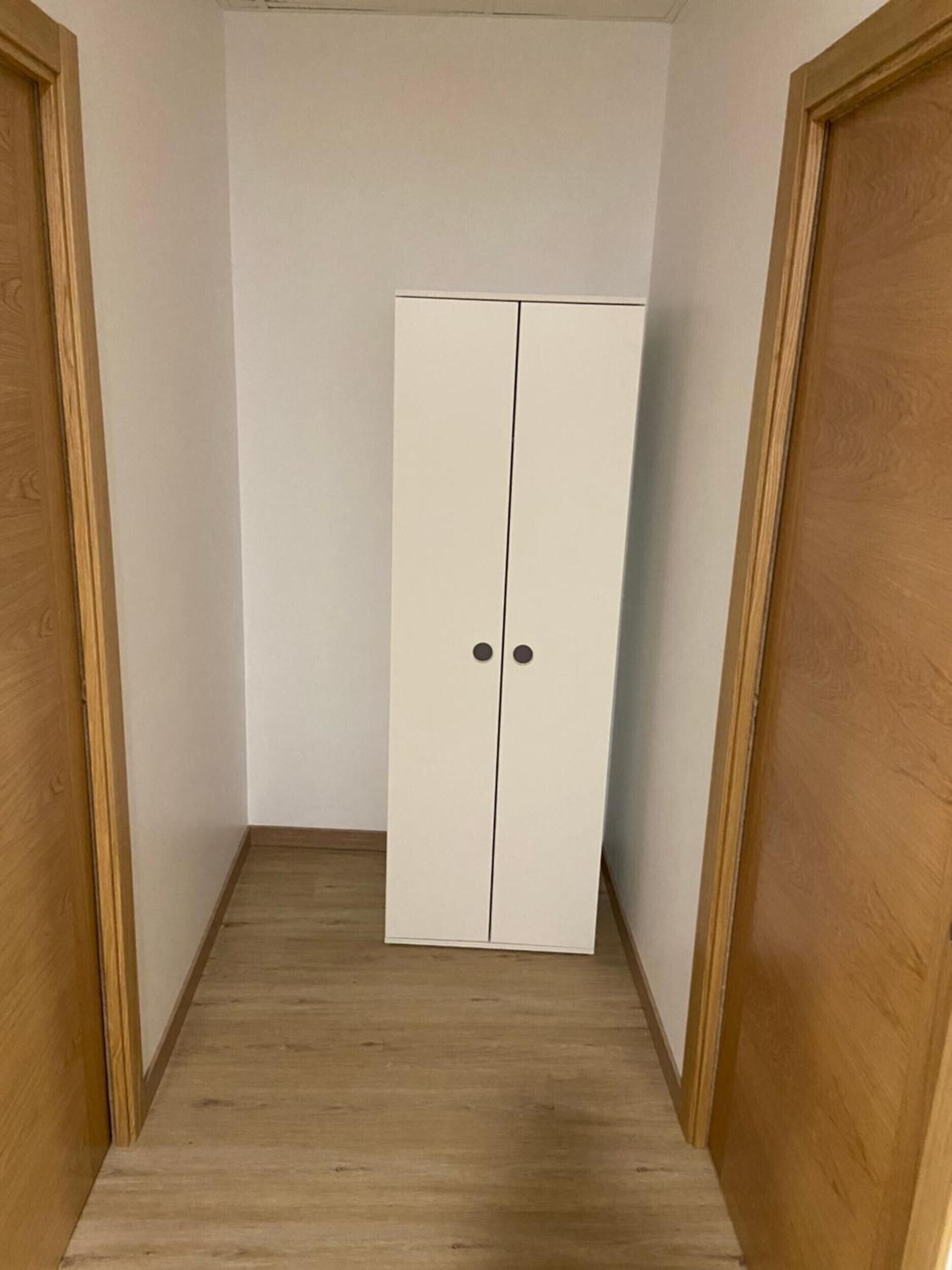 Ein schmaler Flur mit einem weißen Kleiderschrank und Holztüren.
