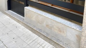 Une entrée moderne, avec un portail en métal noir, une porte en bois et un rebord en pierre.