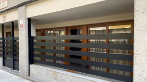 Une façade d’immeuble avec une entrée fermée par un portail, une enseigne et une fenêtre donnant sur l’intérieur.