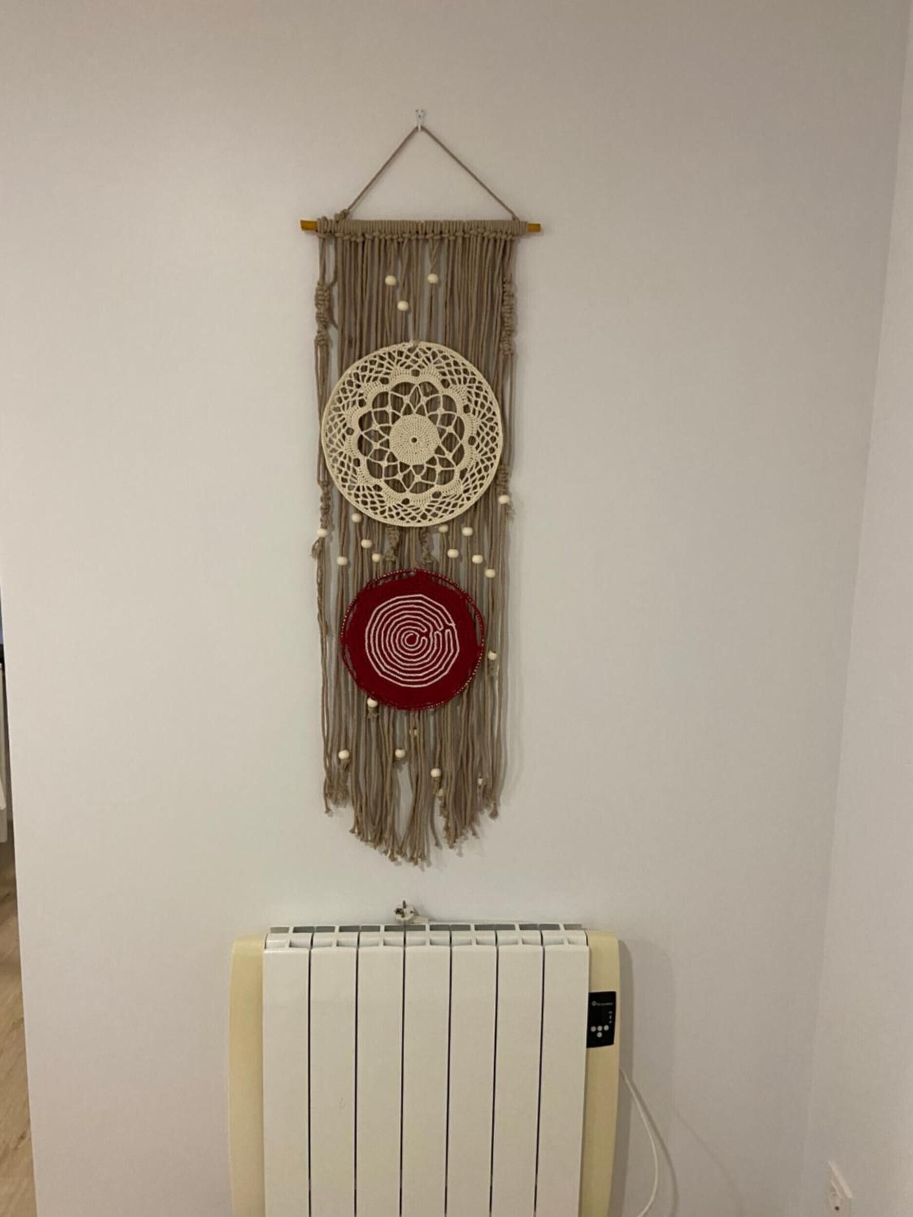 Une décoration murale en macramé, fixée au mur, avec des motifs circulaires et un radiateur en dessous.