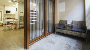 Une pièce dotée d’une porte-fenêtre coulissante, d’un canapé en osier avec des coussins, d’une petite table, d’un four à micro-ondes, d’une échelle et d’un coin repas avec des chaises et une table.