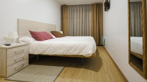 Habitación de hotel con cama, mesita de noche, lámpara, ventilador de techo, televisor y ventana con cortinas.