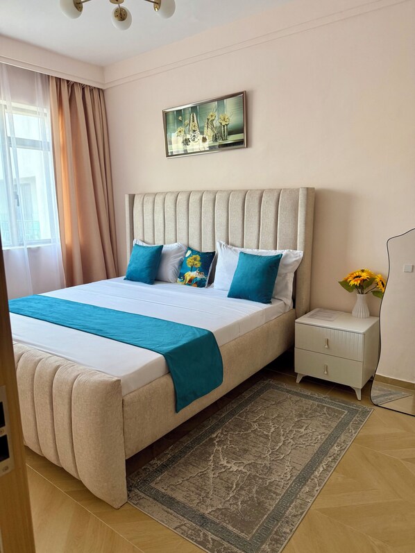 A bedroom with a large bed, a nightstand, a painting, and a window with curtains.