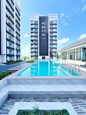 A modern building with a central pool, surrounded by a landscaped area and other buildings.