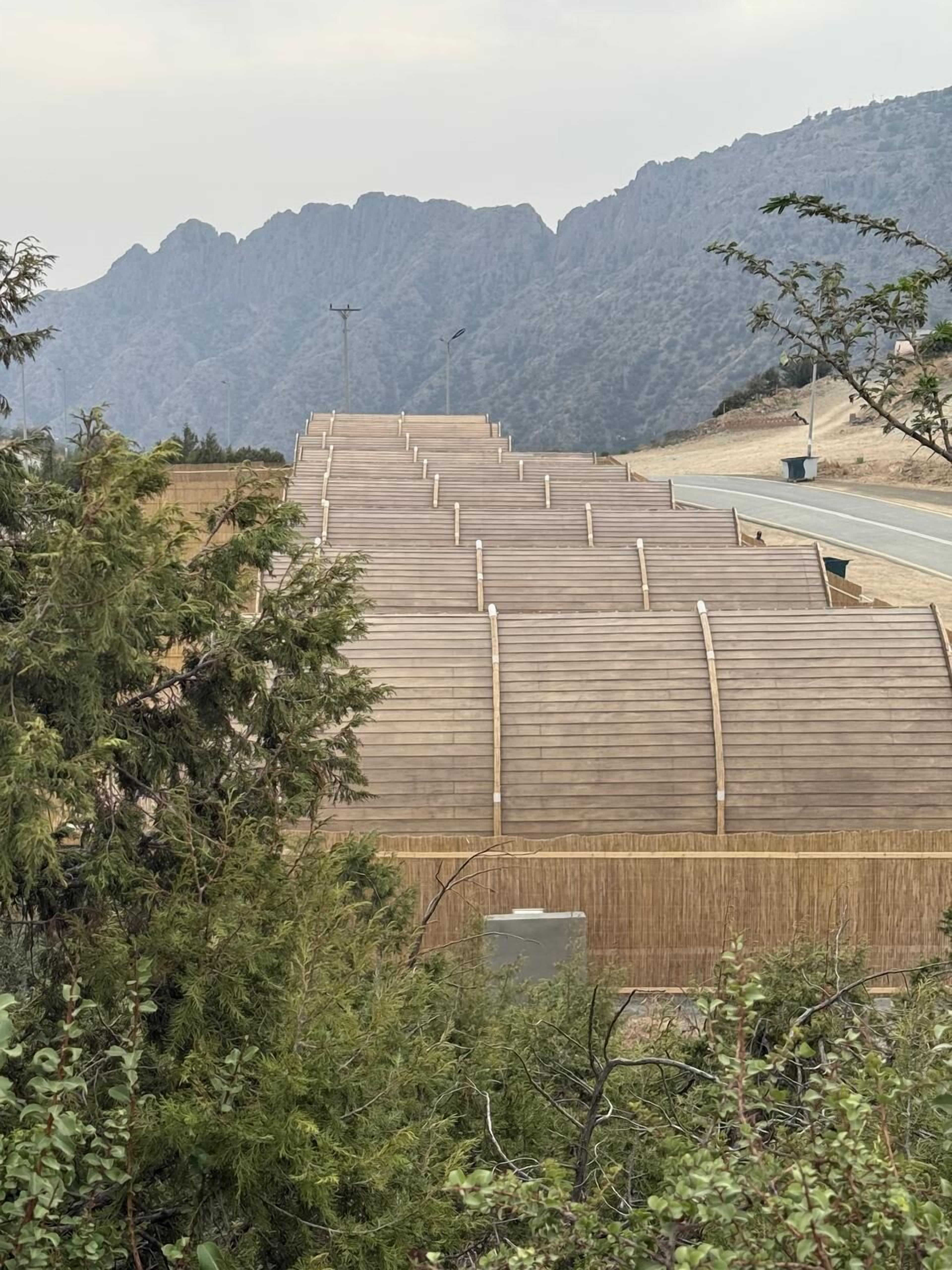 Una hilera larga de estructuras de madera, posiblemente cabañas o varios edificios pequeños, con una carretera y montañas al fondo.