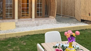 A rustic wooden house with a large arched window and a dining table with chairs and a vase of flowers. - Makamaya (Al Baha)