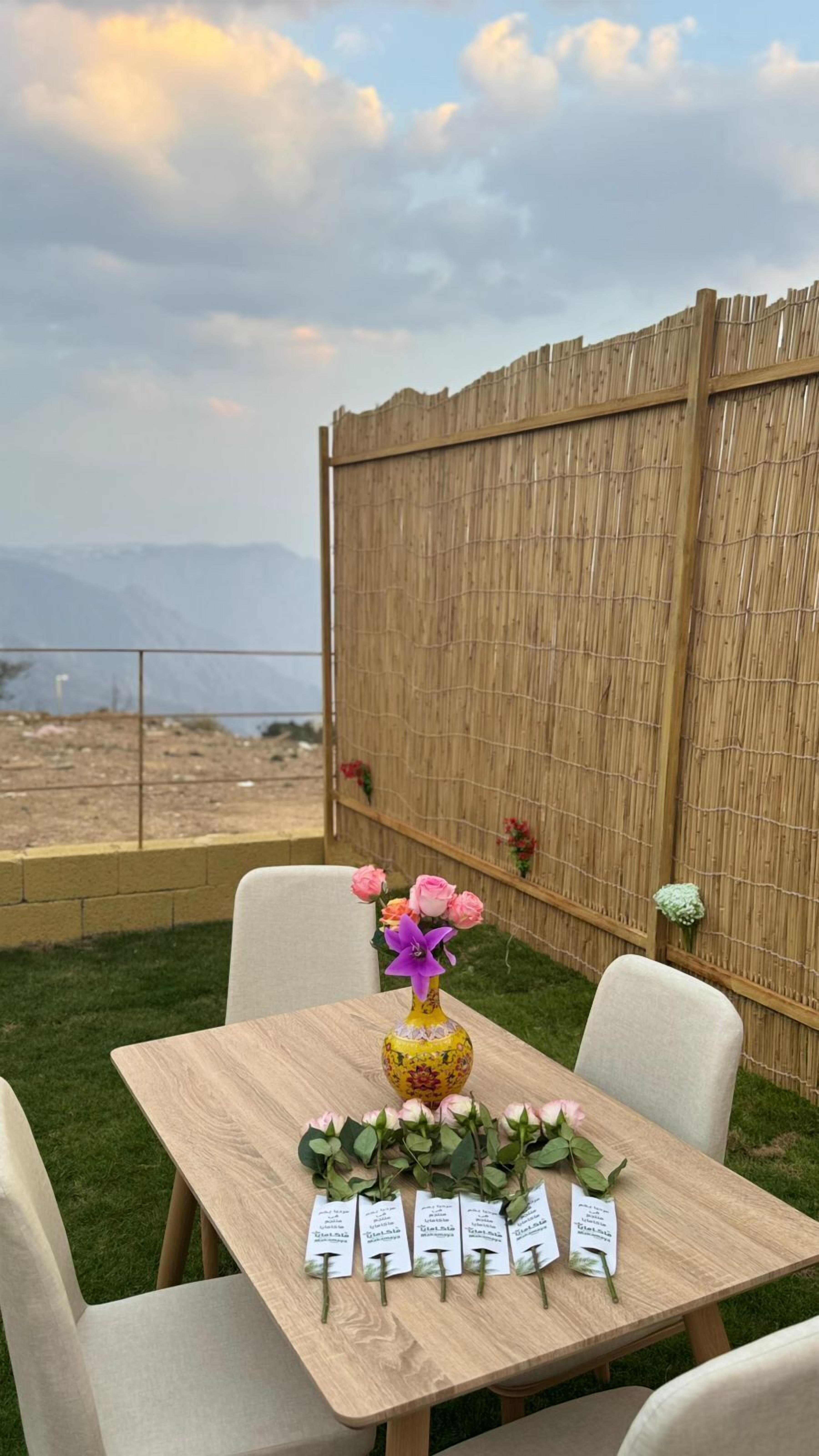 Une table en bois avec des chaises, un vase rempli de fleurs et des étiquettes nominatives posées sur la table.